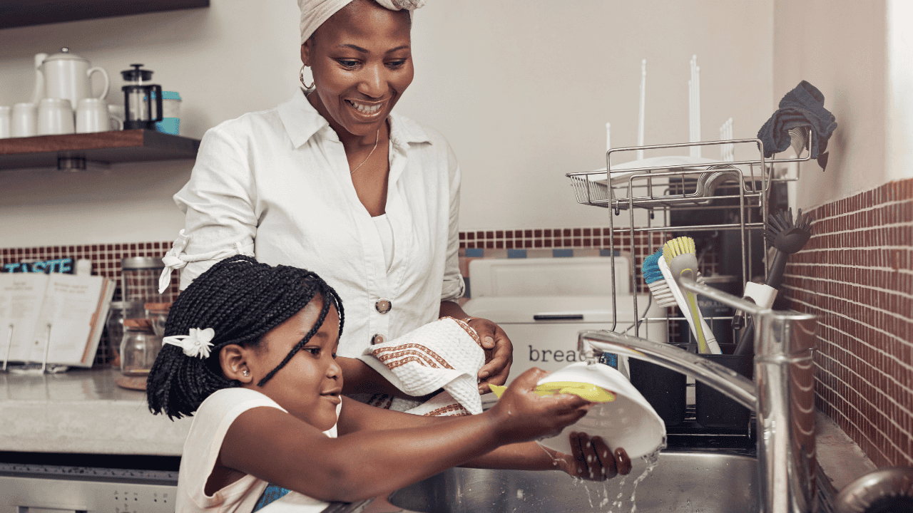 Mother and daughter washing dishes together. Mother is smiling like watching her daughter.